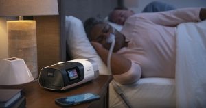 CPAP machine and heated tubing beside a sleeping user, illustrating a setup checked for rainout